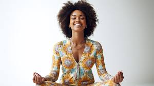 A smiling woman sits cross-legged in meditation, practicing mindfulness to reduce stress. Mindfulness is often encouraged alongside therapy for anxiety in Brooklyn, NY. Clients working with a black therapist in Brooklyn, NY or an online therapist in Brooklyn, NY can learn tools to manage emotions.