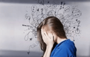 A woman covers her face as chaotic scribbles and question marks swirl around her head, reflecting the overwhelm of anxiety symptoms in Brooklyn, NY — an attachment style therapist in Brooklyn, NY at SG Wellness can help.