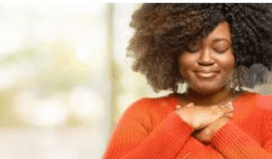A Black woman smiles serenely with hands over her heart, reflecting the self-compassion and peace that anxiety therapy Brooklyn helps build — connect with a BIPOC anxiety therapist in Brooklyn, NY at SG Wellness.