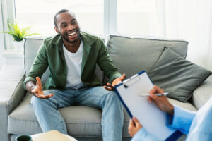 A smiling man talks with his therapist during a schema focused therapy session in Brooklyn, NY, highlighting the supportive approach of a skilled schema therapist in Brooklyn, NY who offers schema therapy online in Brooklyn, NY