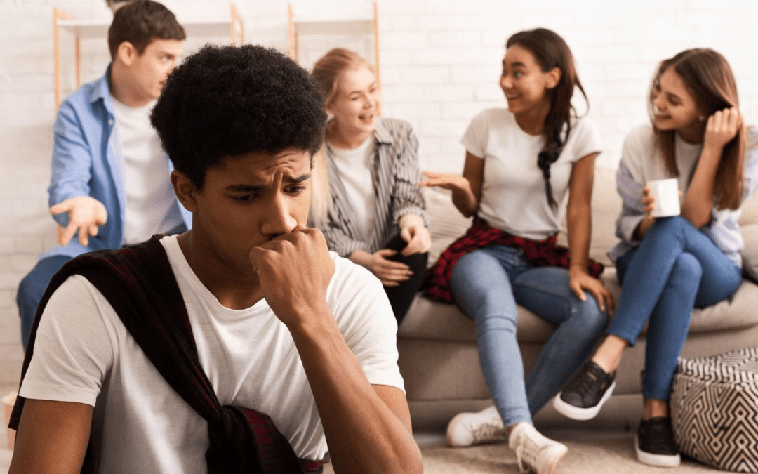A young man sits apart from his laughing peers with a worried expression, capturing the social anxiety and isolation that dealing with self-esteem issues in Brooklyn, NY can create. Low self-esteem often makes ordinary social situations feel threatening, leading to withdrawal and fear of rejection. Working with a self-esteem therapist in Brooklyn, NY can help individuals identify these patterns and begin building the confidence to connect more freely.
