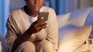 A person sits up in bed at night, lit by the glow of the phone in their hands as they scroll. Late-night comparison like this often deepens the sense of feeling stuck in Brooklyn, NY. A young adult therapist in Brooklyn, NY and an attachment style therapist in Brooklyn, NY can help break the cycle of comparison and self-doubt. 
